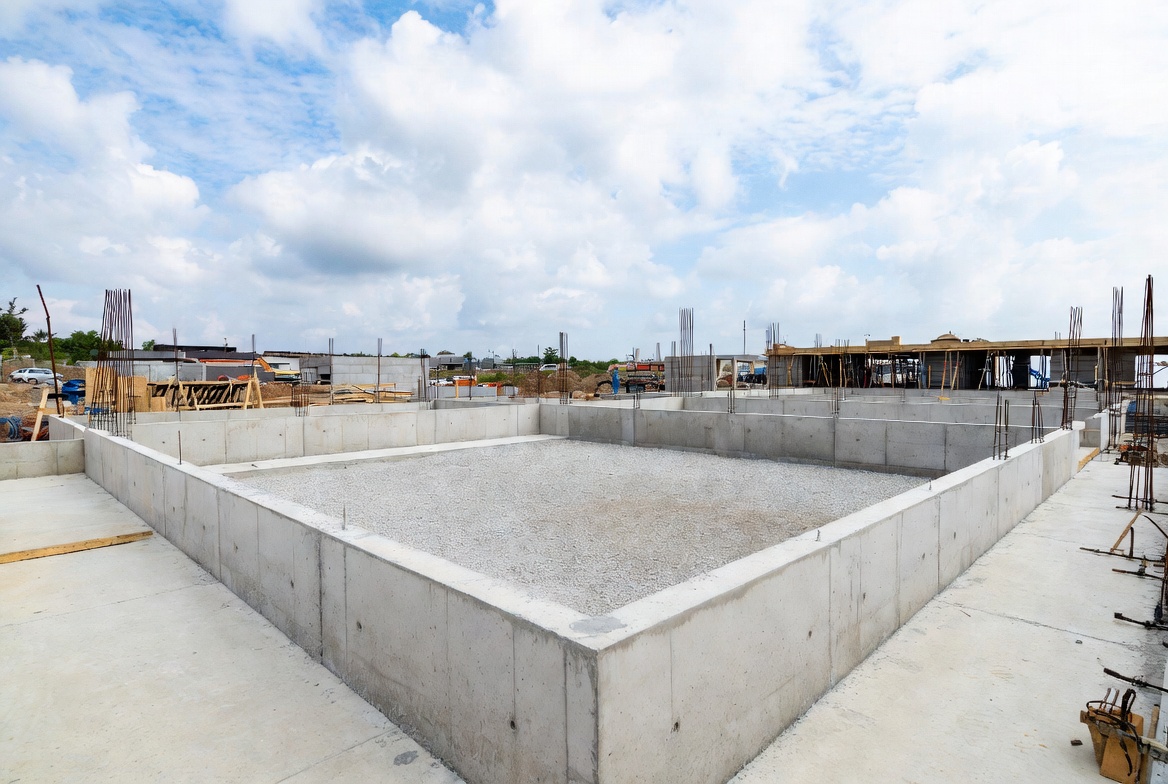 Reinforced concrete foundation enclosure with gravel base and vertical reinforcing bars on site.