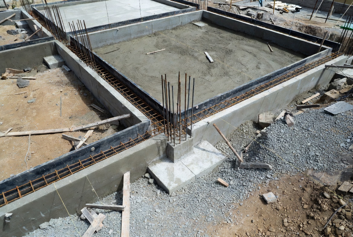Reinforced concrete foundation under construction with exposed rebar, footing beams, and slab area.