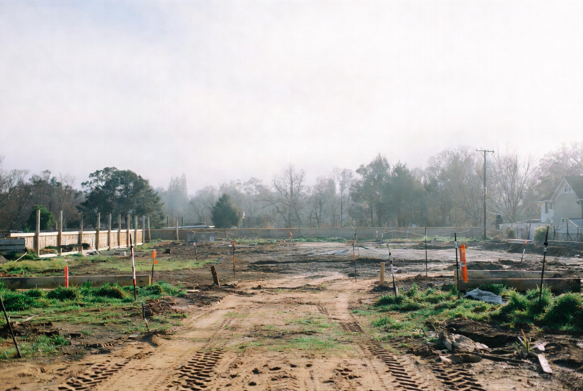 Residential site with staking, graded pads, and early concrete access work before house construction begins.