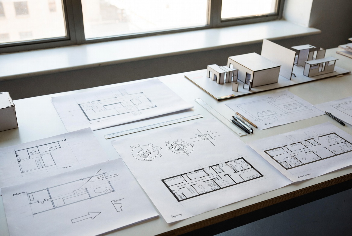 Space planning study with floor plans, bubble diagrams, and architectural study models on a studio desk.
