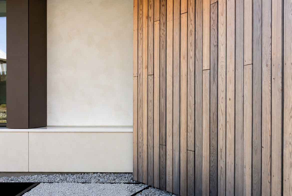 Facade detail combining vertical timber cladding, mineral render, and gravel drainage at a modern building.
