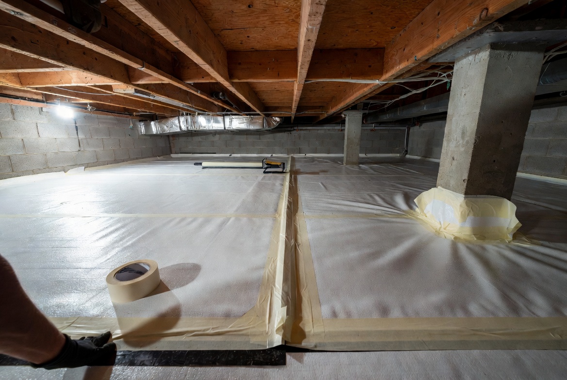 Crawl space vapor barrier tape being applied across seams during installation.