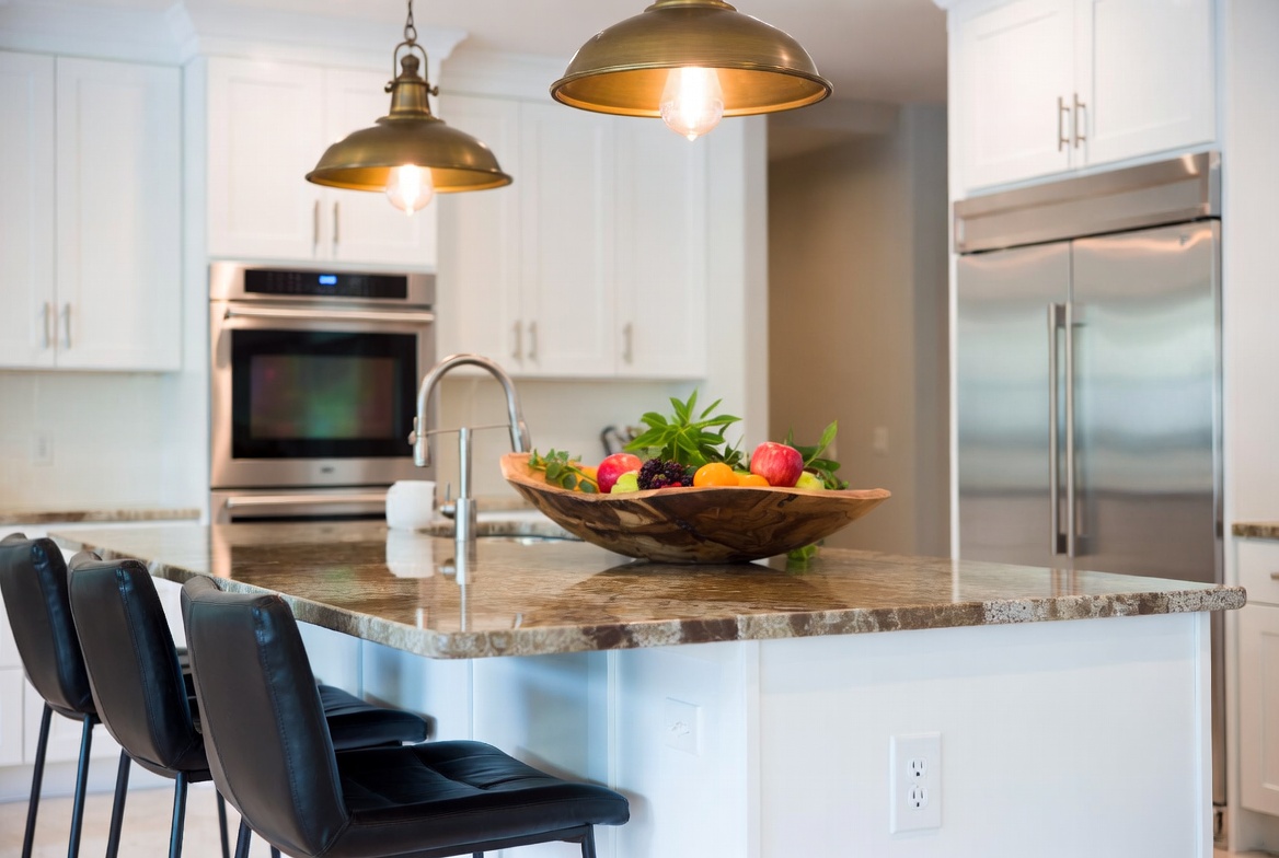 Stylish kitchen island with white cabinets below and rich brown granite waterfall countertop.