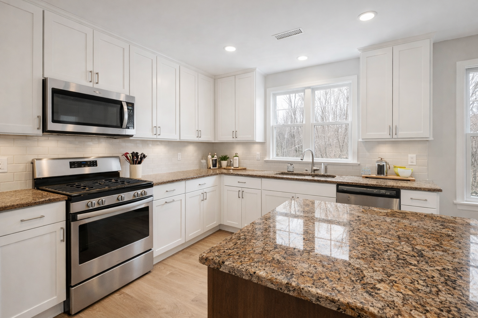 White kitchen cabinets paired with brown granite counters in a bright L-shaped kitchen.