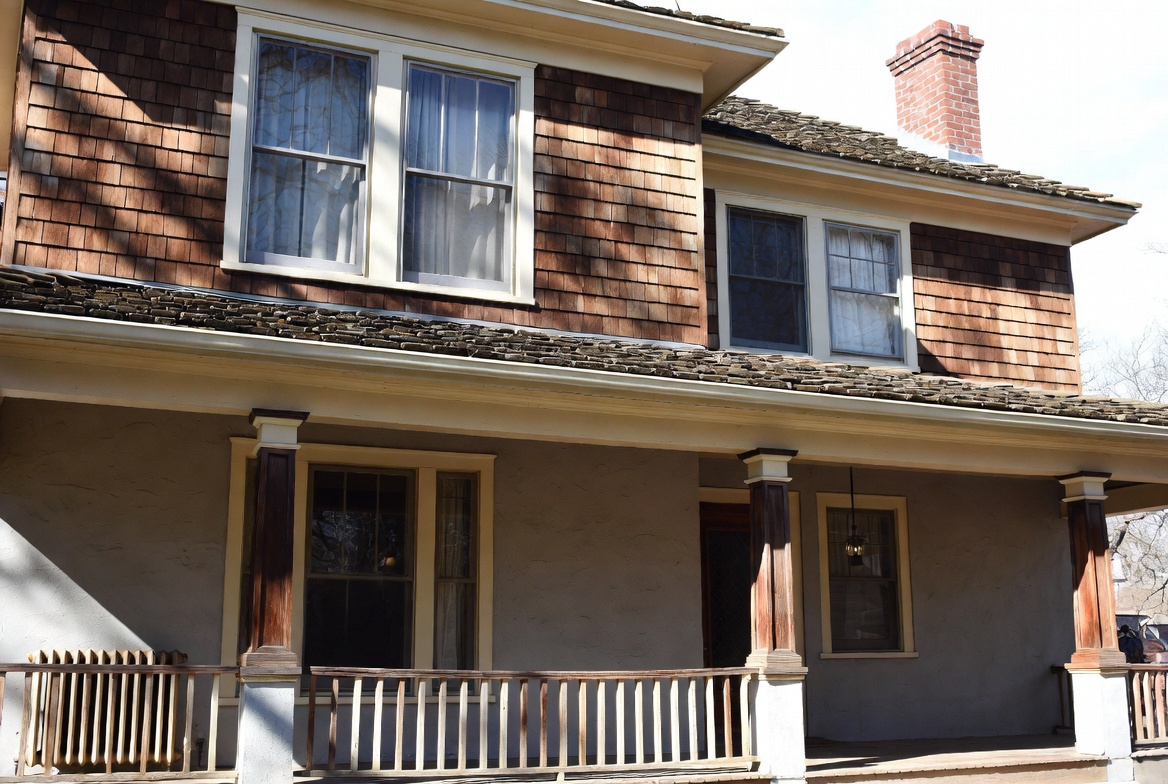 Authentic 1910s American house with front porch, wood shingles, brick chimney, and double-hung windows.