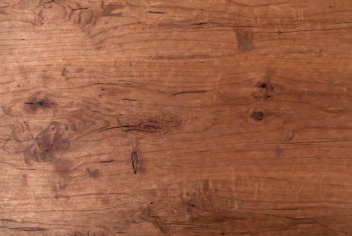 Close-up of mahogany wood grain showing warm brown-red color, knots, and natural figure.