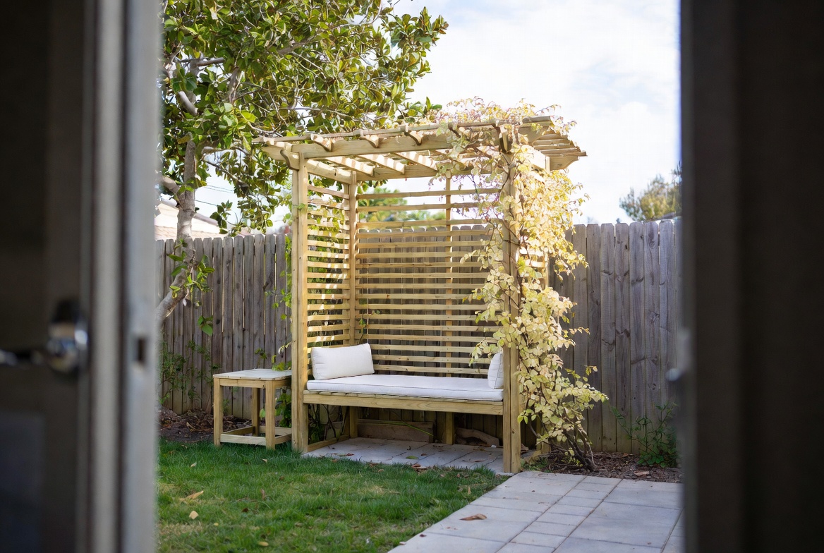 Small backyard bench under a simple pergola with vines and a compact paved sitting area.