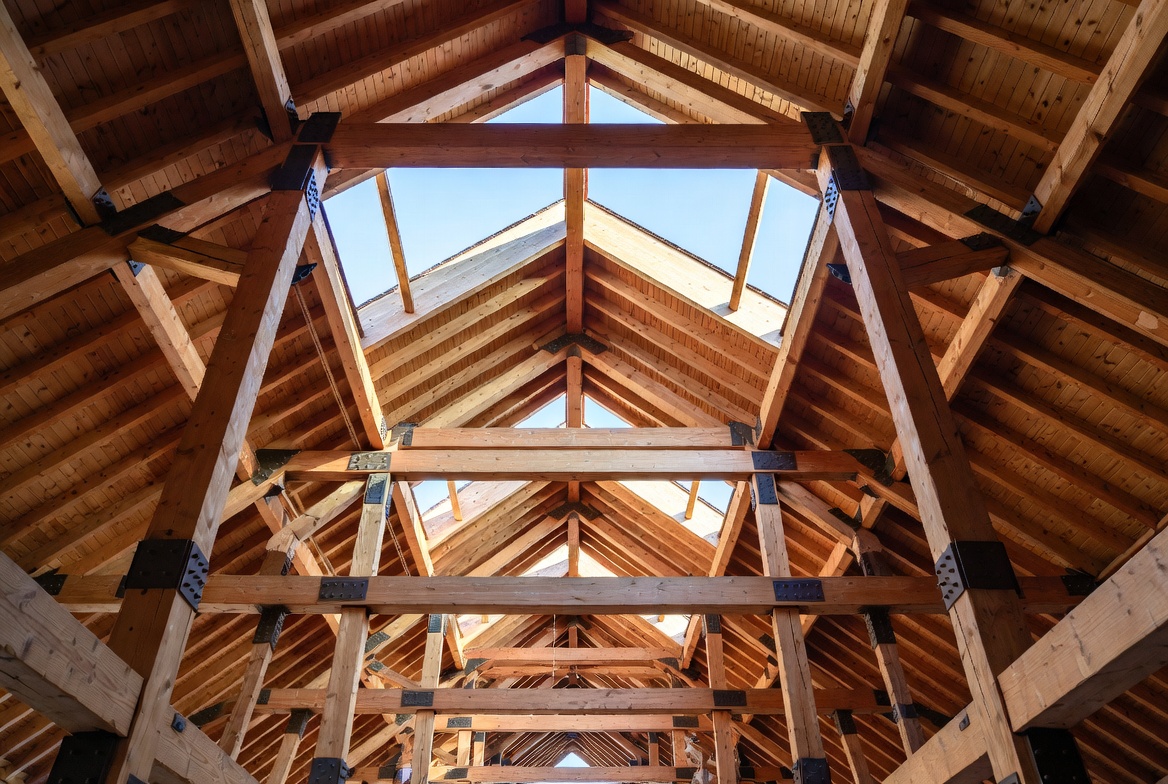 Series of timber trusses spanning a large interior with repeated frames and visible steel plates.