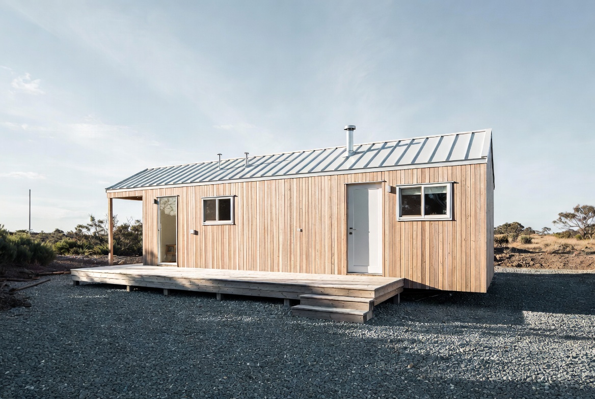 Long narrow tiny home with timber cladding, front deck, and metal roof.