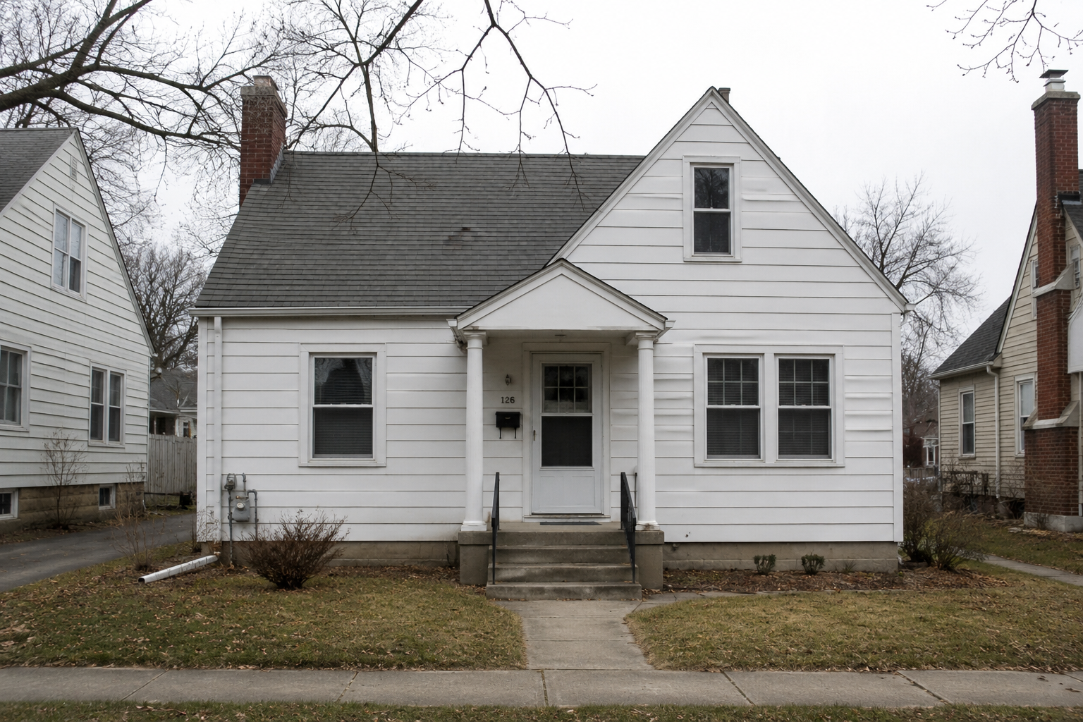 Modest 1940s white house exterior with simple gable roof, small entry porch, and older neighborhood setting.