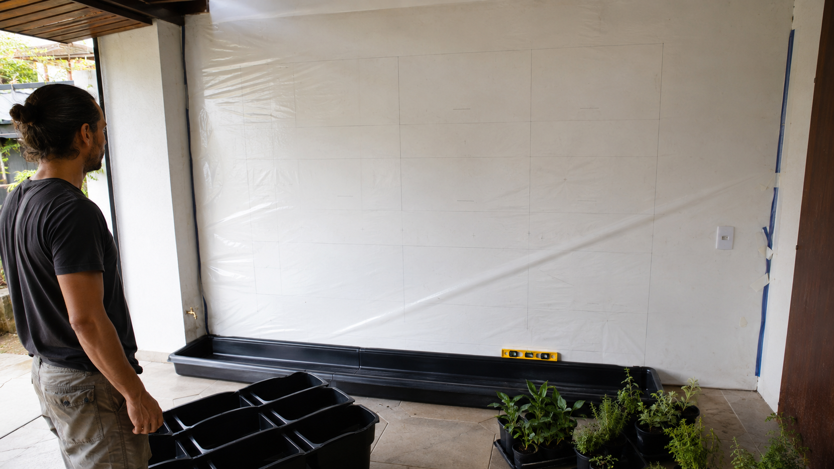 A vertical garden installation being planned with wall protection, planter modules, water tray, and plants nearby.