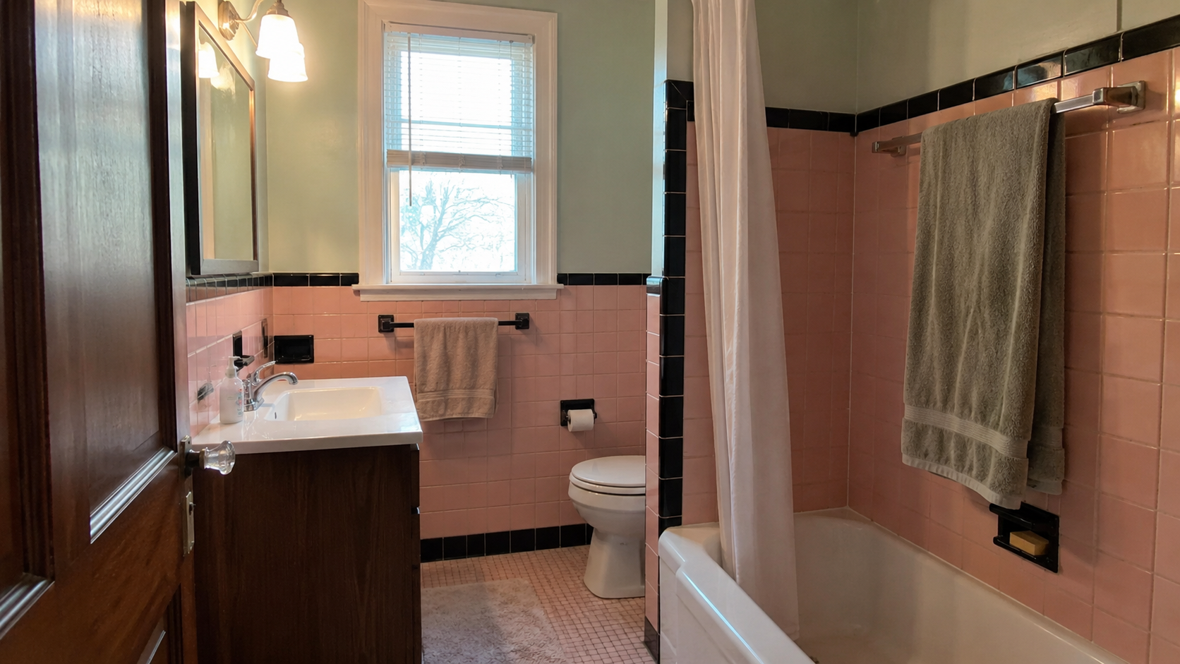 Original 1950s pink bathroom tile kept during a remodel with updated vanity, lighting, and fresh paint.