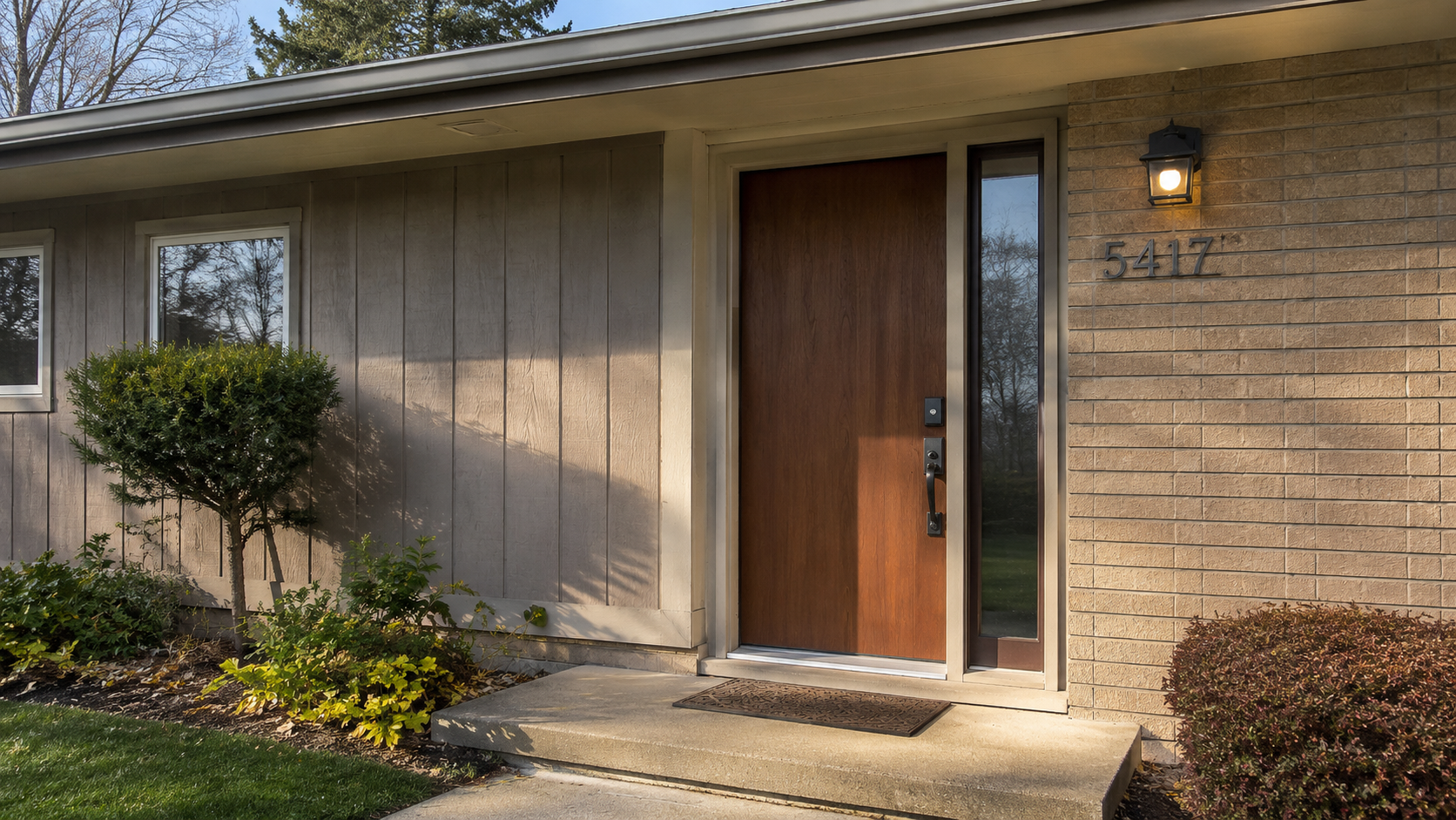 Updated 1970s front door with wood slab, sidelight, brick, modern hardware, and entry lighting.  Caption A good 1970s front door tells you more than the door style; the glass,