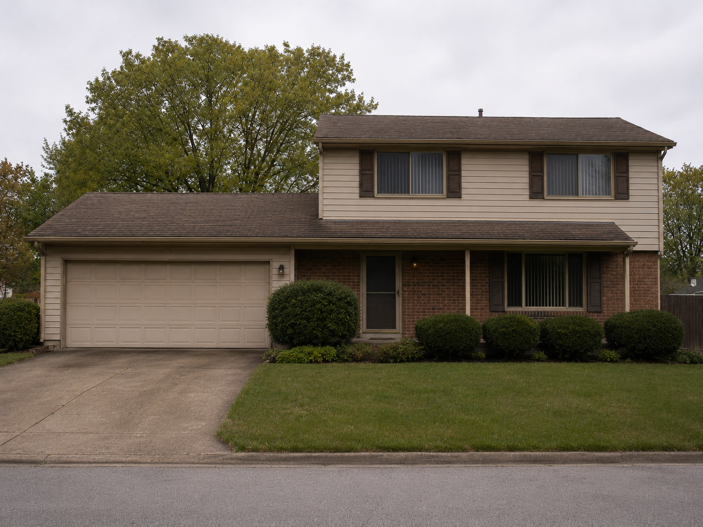 1980s suburban house exterior with beige siding, brick veneer, brown shutters, garage, lawn, and shrubs.