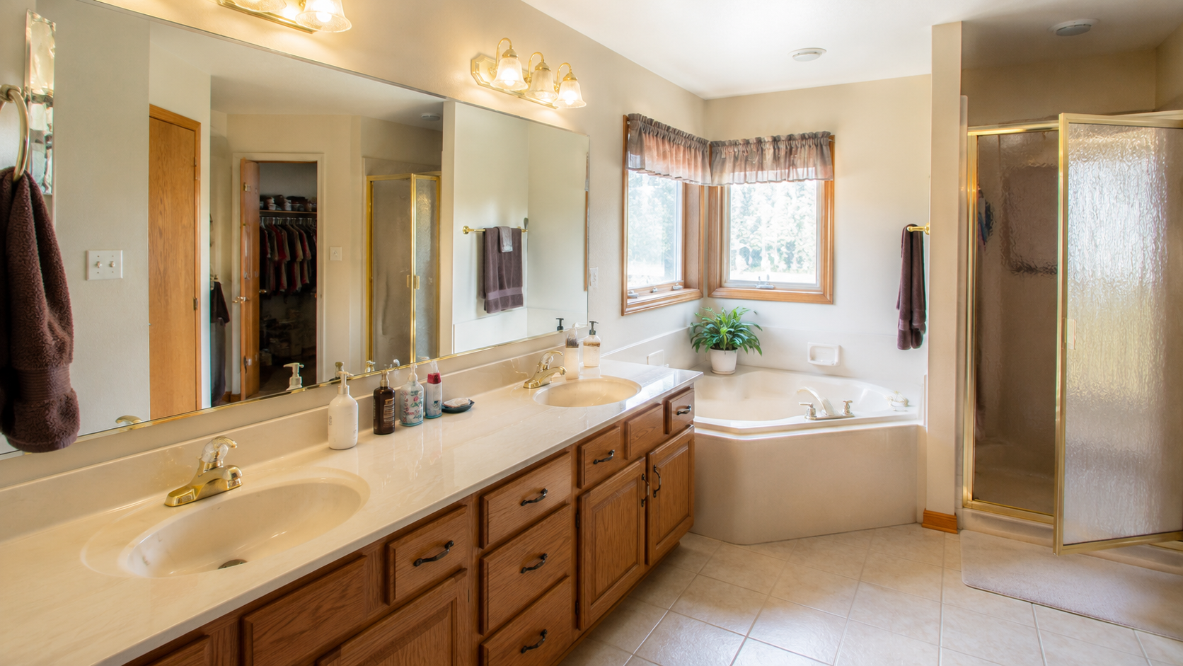 1990s bathroom with long oak vanity, cultured marble counter, large mirror, corner tub, and shower.