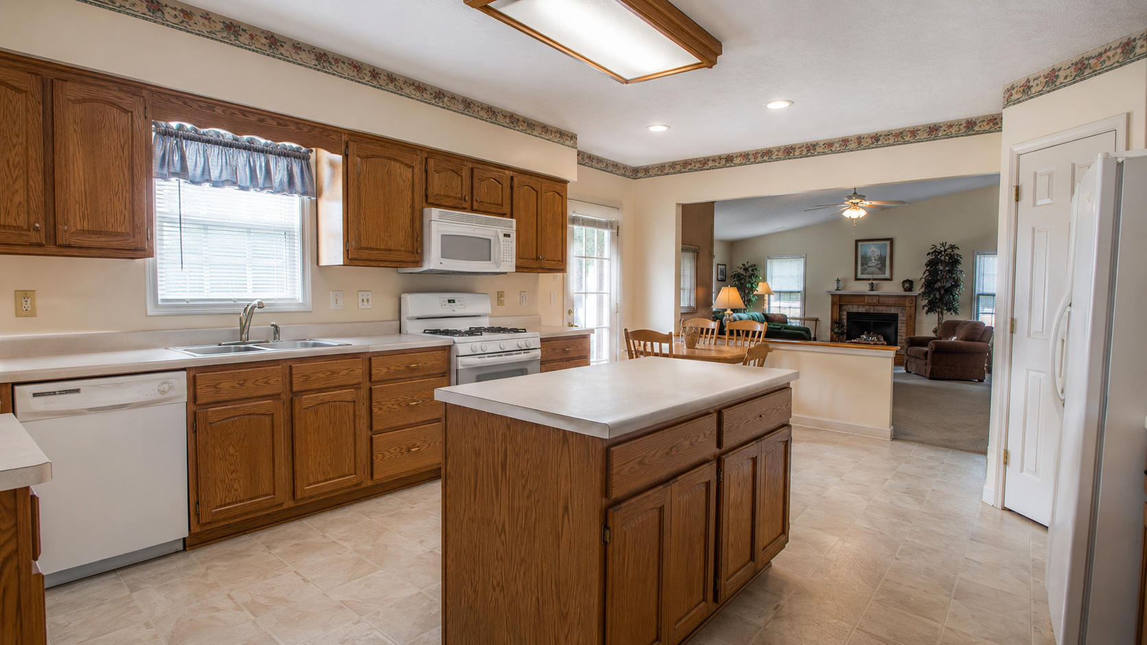 1990s kitchen before remodel with oak cabinets, laminate counters, island, and dated lighting.