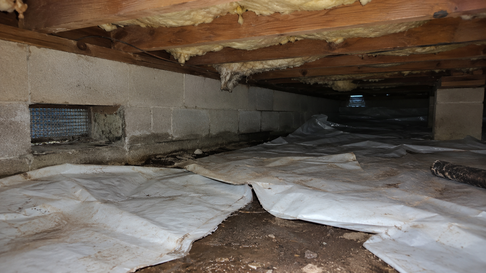 Poor crawl space encapsulation with loose vapor barrier, open seams, unsealed wall edges, exposed vent, and damp soil.