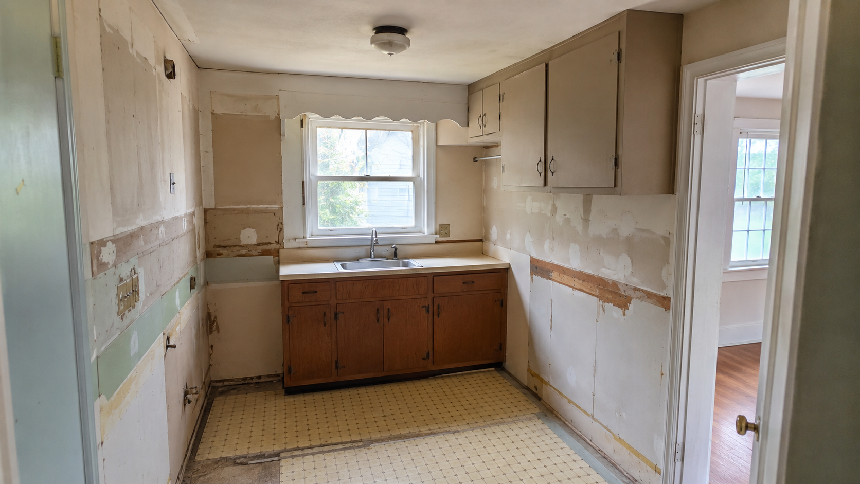 Cape Cod kitchen during remodeling with removed cabinets, sink window, patched walls, and old flooring.