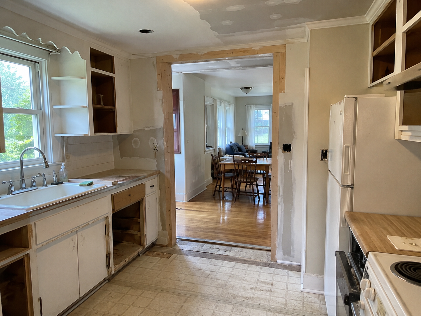 Small Cape Cod kitchen remodel with widened wall opening, patched ceiling, sink window, and dining room beyond.