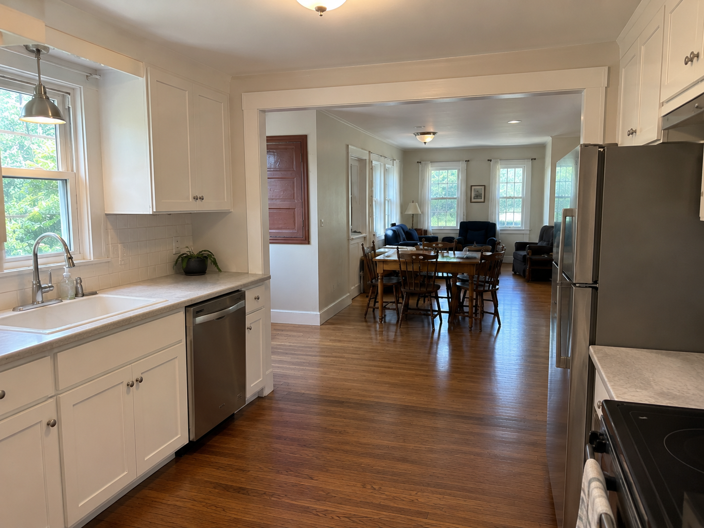 Finished Cape Cod kitchen with widened opening, wood floor, sink window, and dining room beyond.