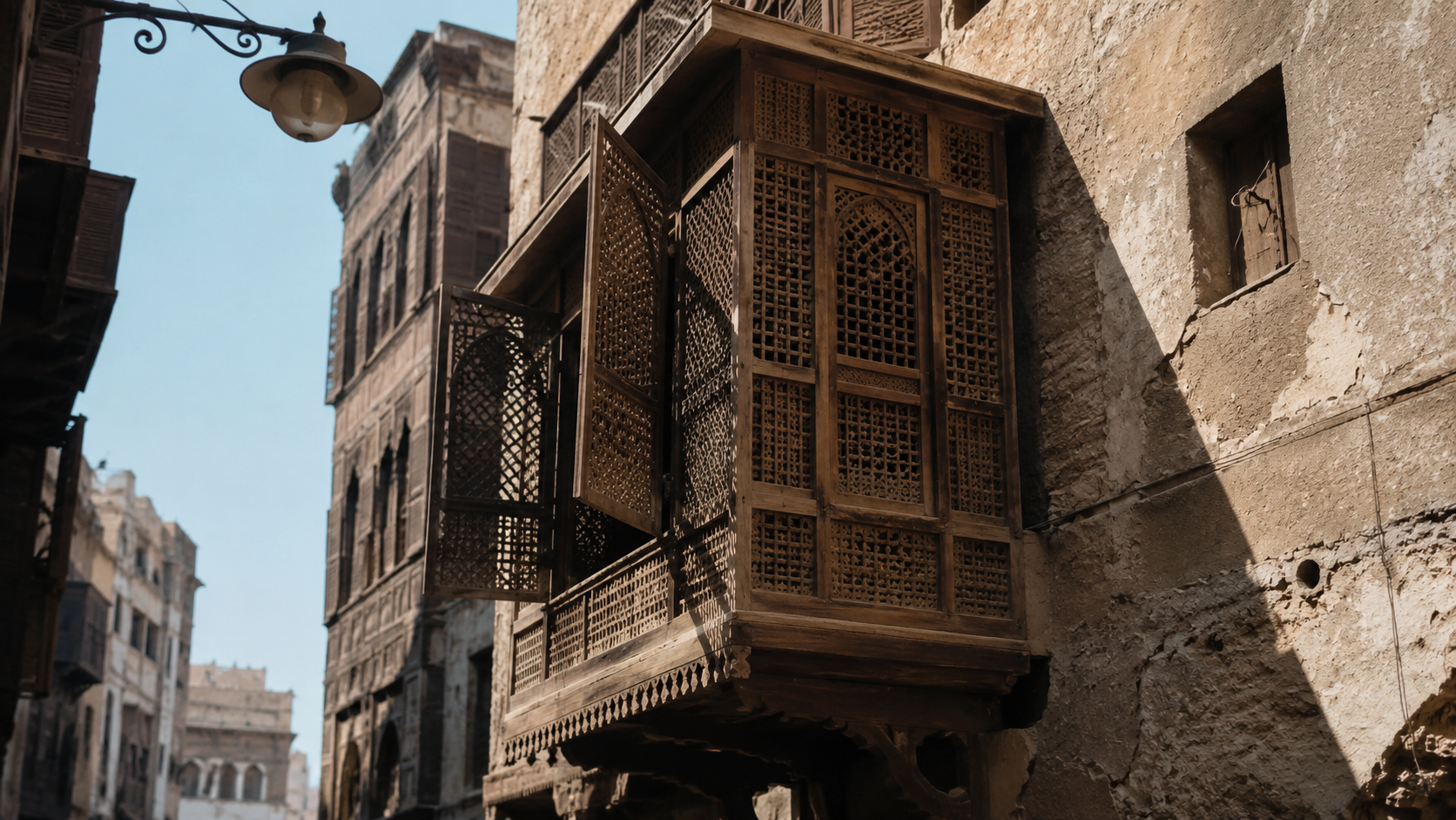 Traditional wooden mashrabiya screen projecting from an upper-floor window and filtering sunlight over a narrow historic street.