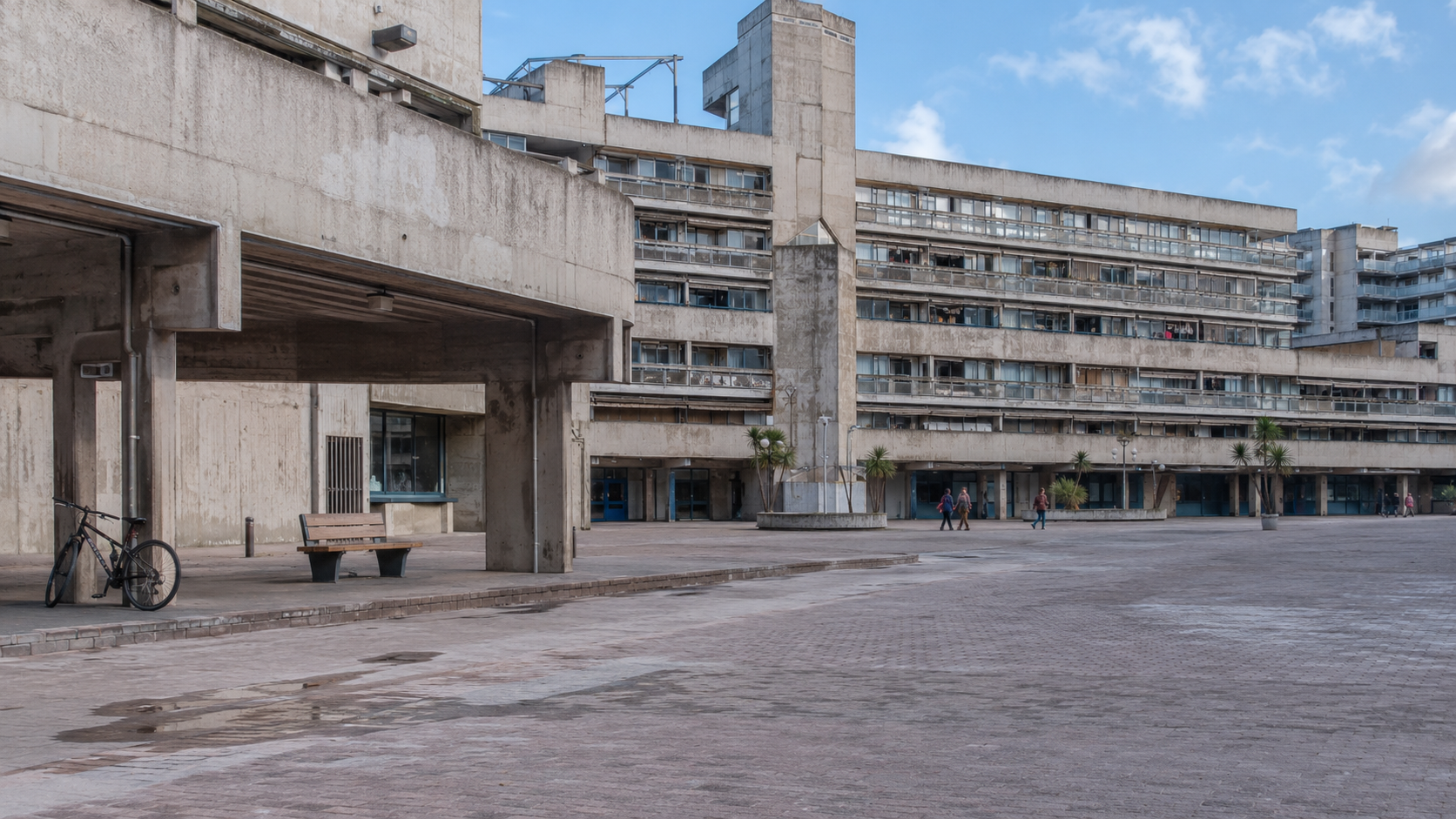 Aging modernist concrete housing or civic complex with patched repairs, staining, repetitive windows, and an underused public space.