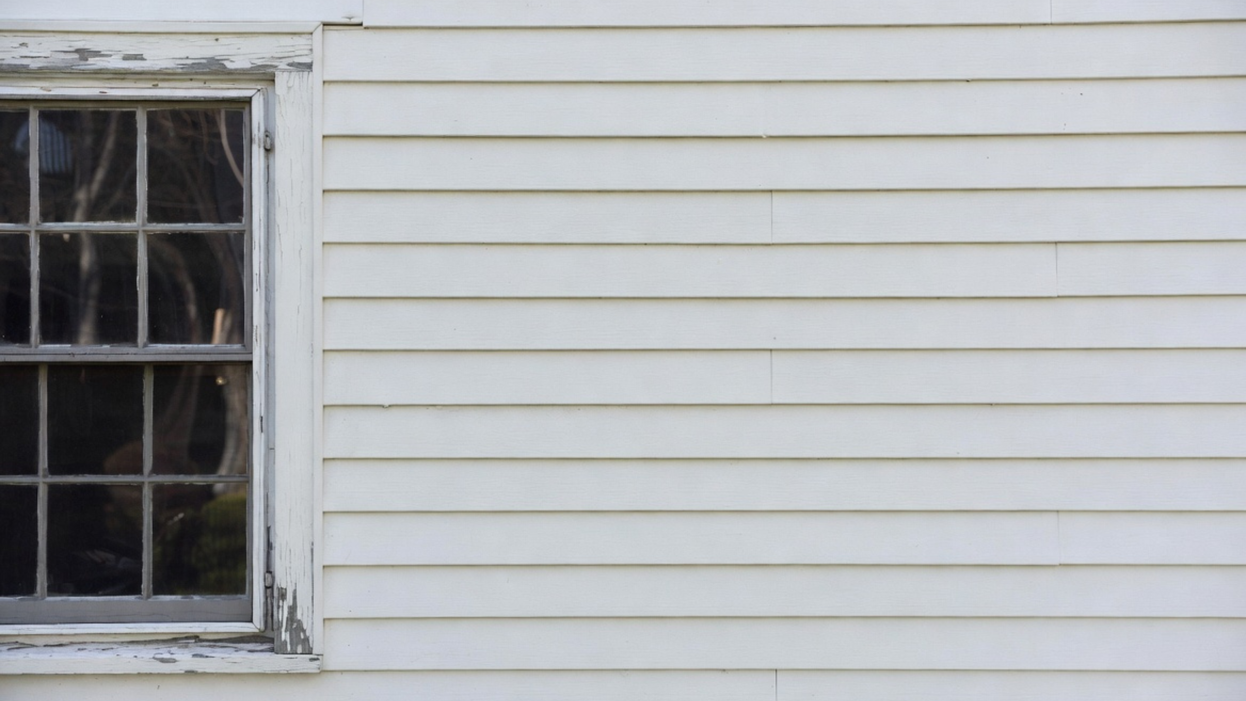 Older window with peeling trim paint beside white siding on a Cape Cod house.