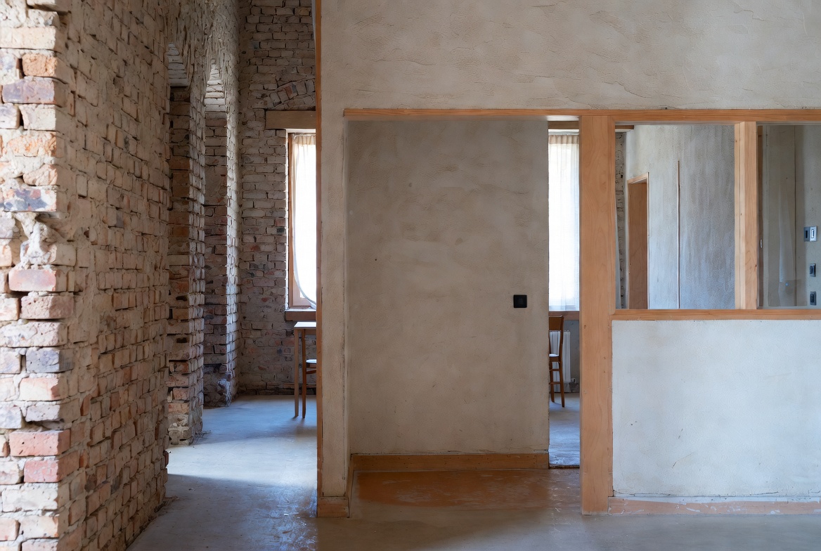 Interior with exposed brick, plaster walls, wood framing, concrete floor, and openings.