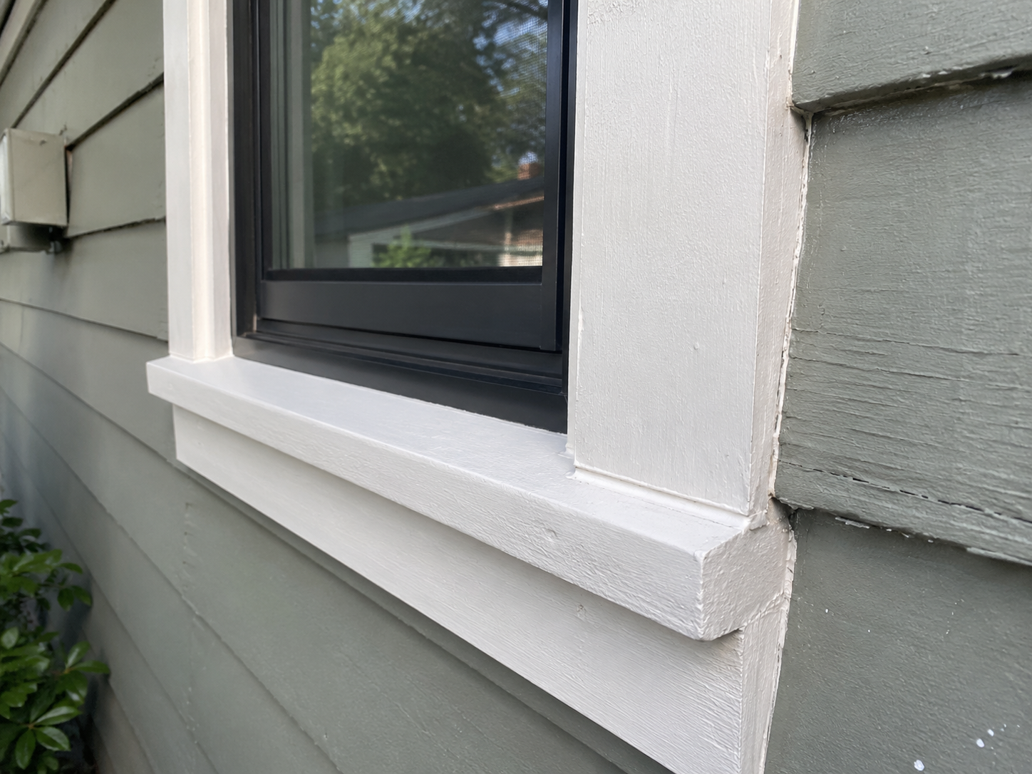 Close-up of replacement window casing, sill, and siding detail in daylight.