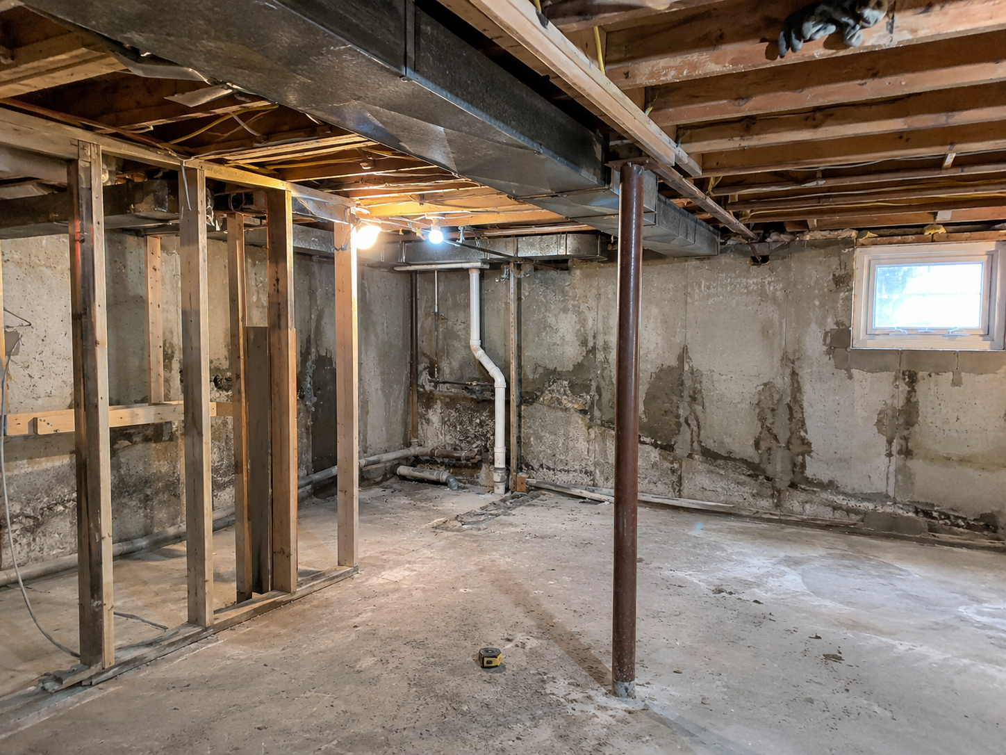 Cape Cod basement remodel with exposed ductwork, plumbing, framing, support post, and foundation wall.