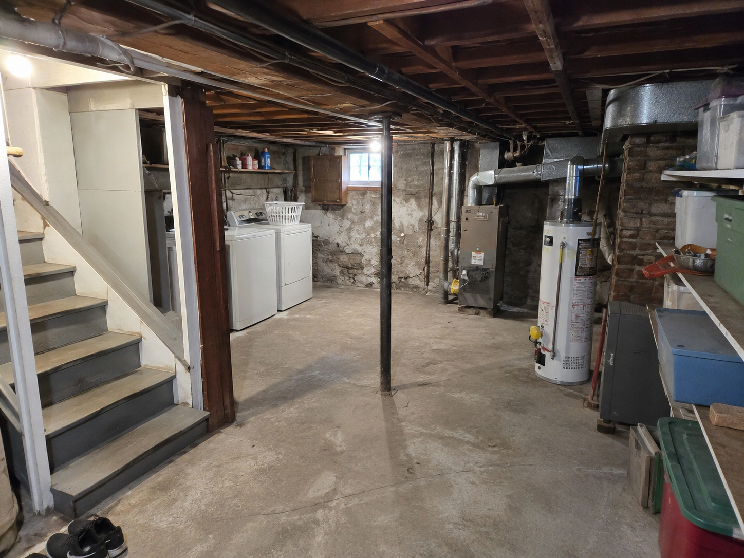 Cape Cod basement before guest-suite planning with low ceiling, laundry, ducts, posts, and utilities.