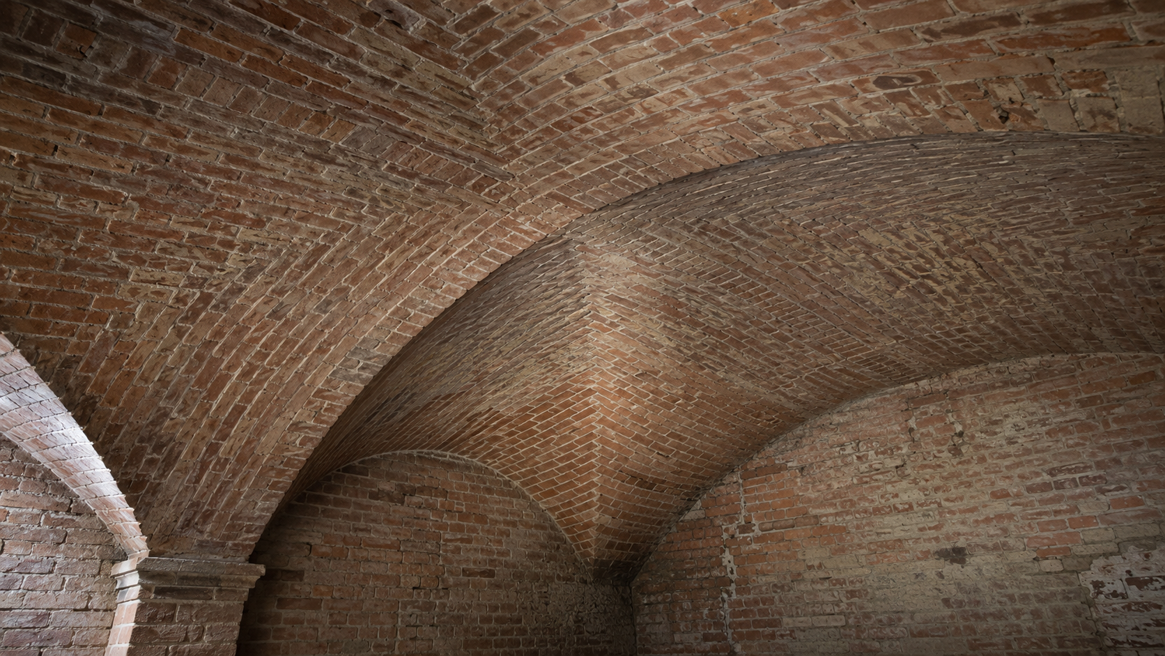 Close view of a brick groin vault showing the diagonal intersection of two curved vault surfaces.