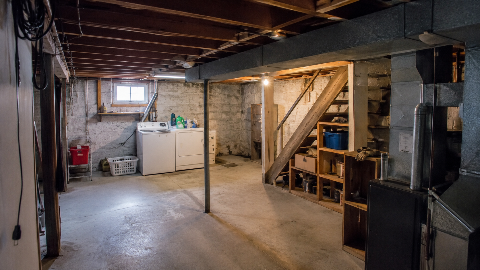 Cape Cod basement before remodel with low ceiling, ducts, stairs, posts, foundation wall, and mechanicals.