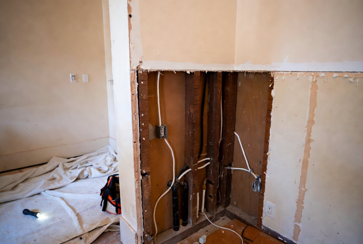 Opened wall in an old house showing wiring and plumbing during renovation.