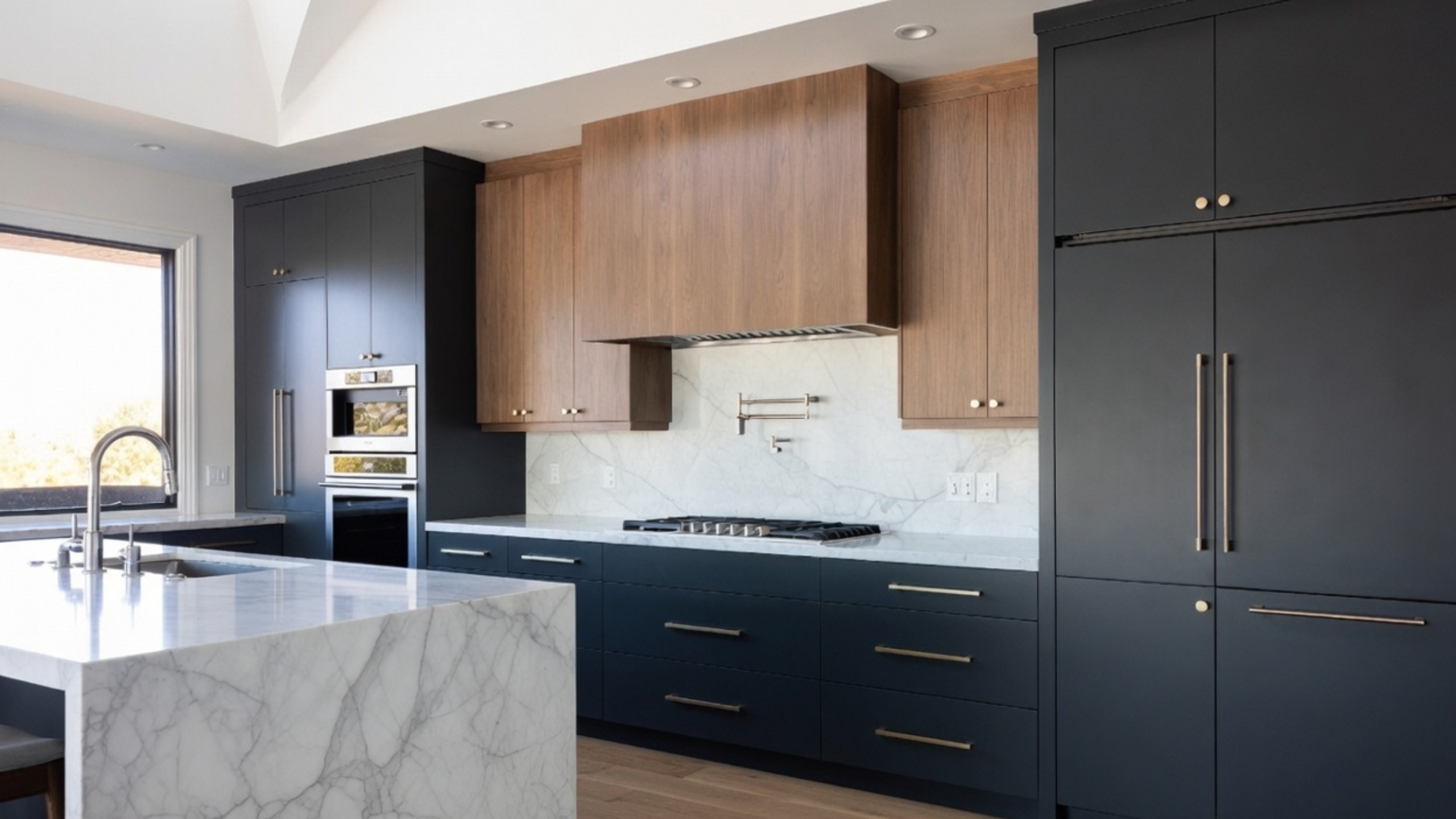 Kitchen combining dark navy cabinets, walnut upper cabinets, white marble and brushed brass hardware.