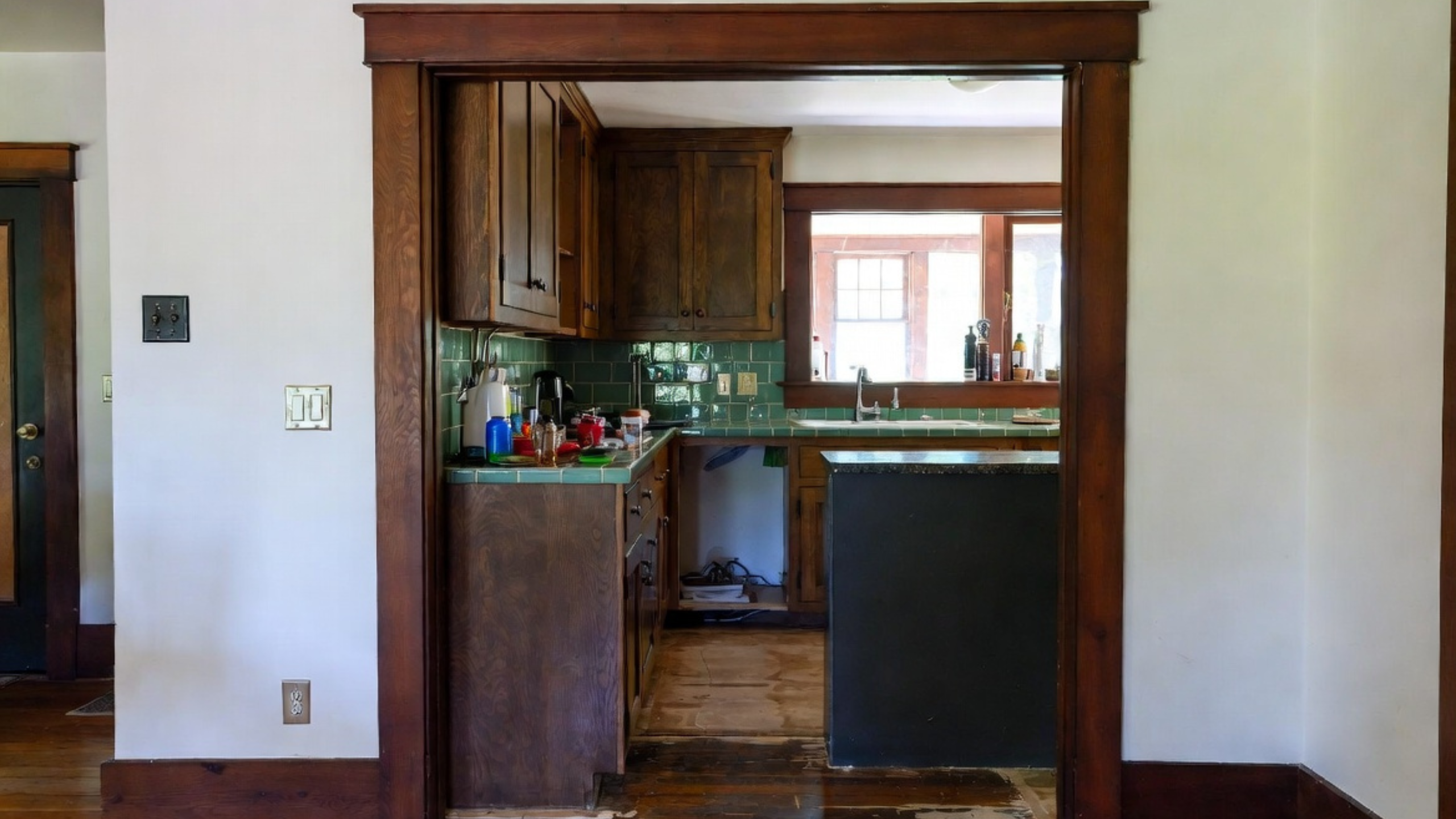 Older Craftsman kitchen with wood trim, green tile, worn floor, and narrow layout.