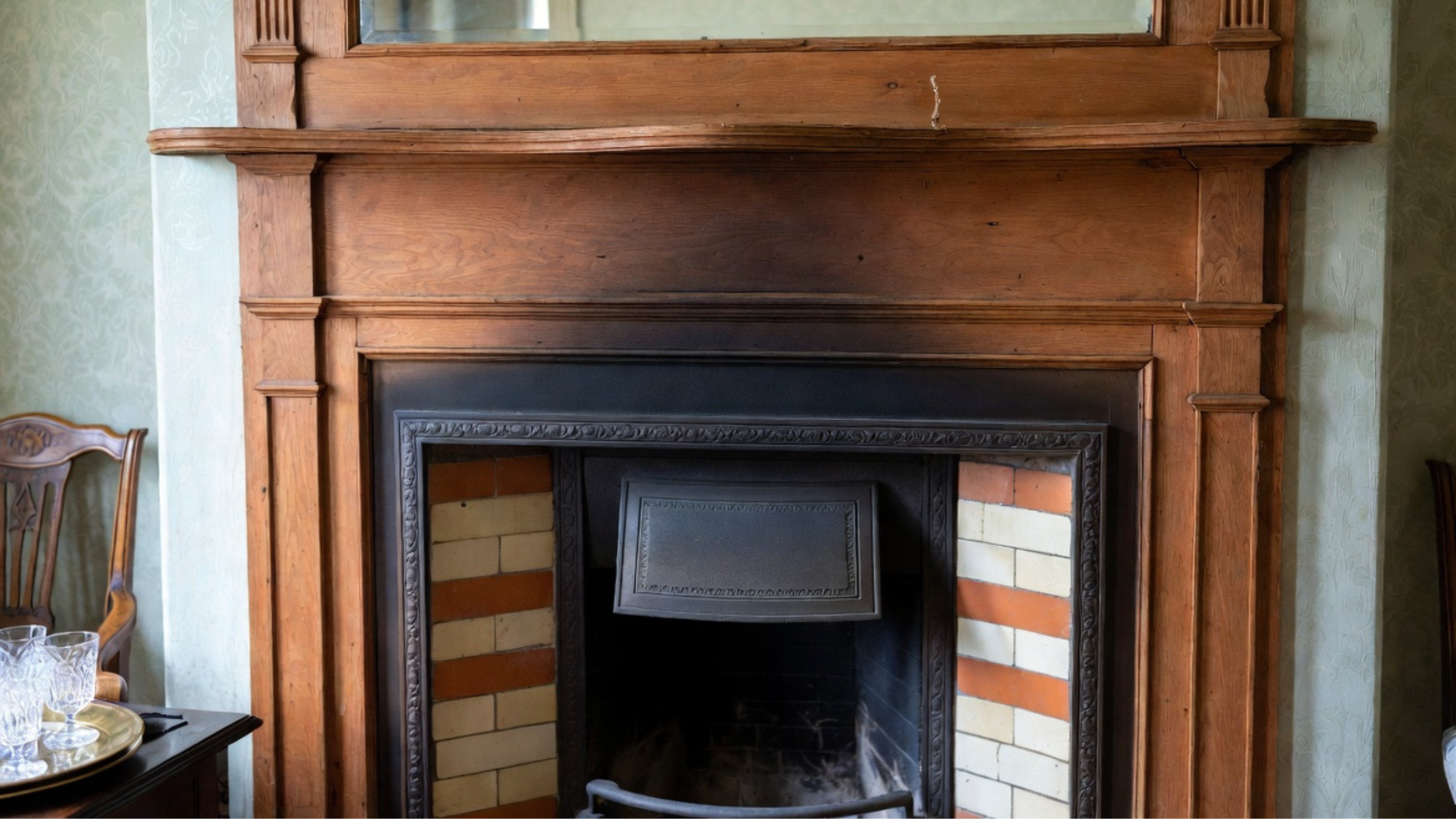 Original wood fireplace mantel with mirrored overmantel, cast-iron insert and decorative tile in a house from around 1900.