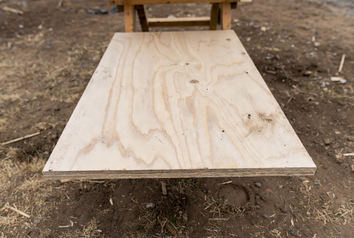 Plywood panel showing layered edges, surface grain, dirt, and minor jobsite wear.