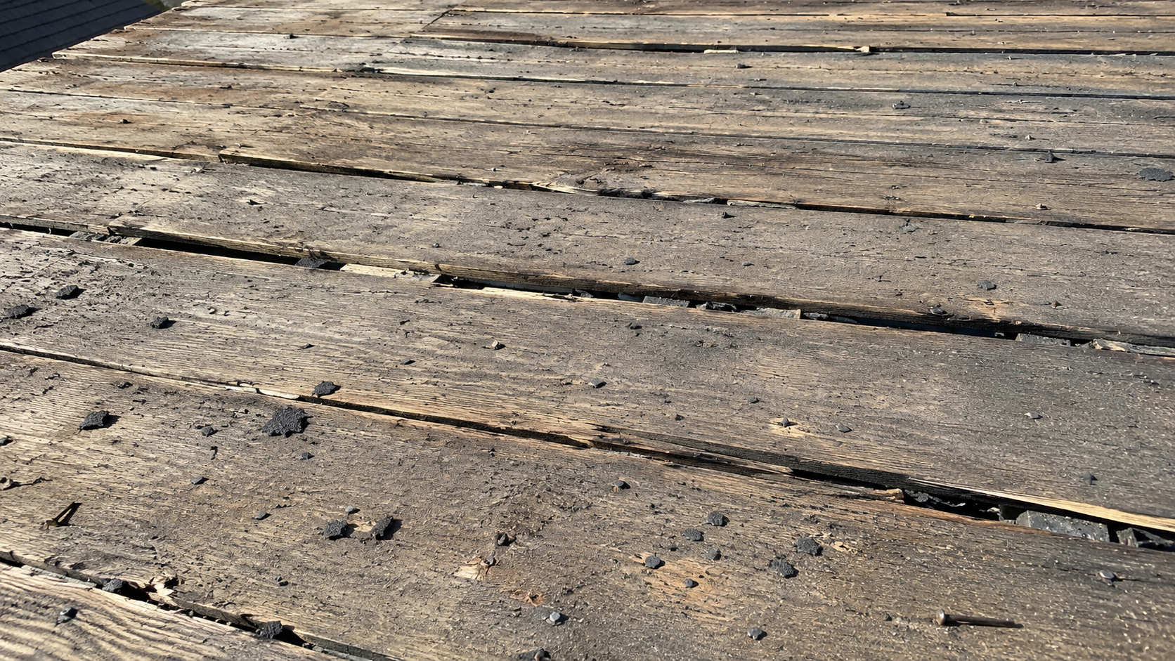 Close view of old roof decking boards with gaps, nail holes, and worn plank edges.