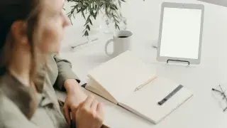 interior designer sitting beside a table with an iPad, paper, and pen, looking distant and confused as if struggling with too many ideas