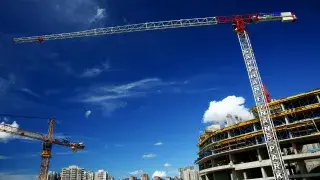 Tower crane at a construction site lifting materials with a clear sky in the background.