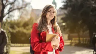 Architecture student standing proudly in front of university with portfolio in hand.