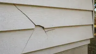 Cracked older house siding with brittle horizontal boards and visible damage.