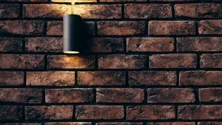 Exterior stone wall with black tubular light fixture.