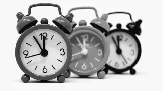 Architecture student adjusting a black twin-bell alarm clock.
