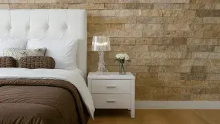 Modern bedroom interior featuring a natural stone accent wall, white headboard, and minimalist decor.