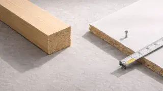 Close-up showing dimensional lumber beside a drywall panel with a tape measure checking thickness