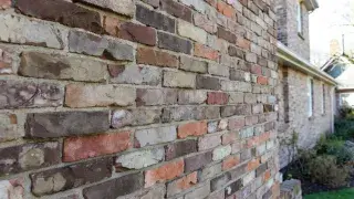 Antique thin brick veneer on modest residential house exterior with reclaimed weathered texture .