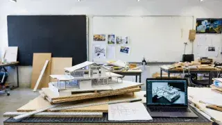Architecture student studio workspace with physical massing models, drawings, and laptop.