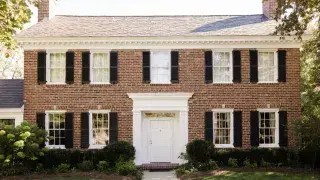 Classic brick colonial house with centered doorway, black shutters, and symmetrical windows.